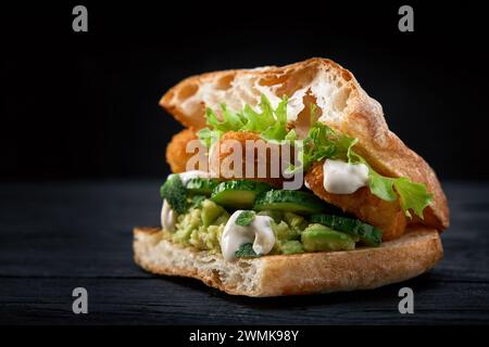 Appetitlich Sandwich auf einem Holzbrett. Baguette Sandwich mit Füllung aus Kopfsalat, Scheiben Tomate. Dunklen Hintergrund. Blick von oben. Close-up. Stockfoto