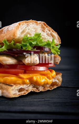 Appetitlich Sandwich auf einem Holzbrett. Baguette Sandwich mit Füllung aus Kopfsalat, Scheiben Tomate. Dunklen Hintergrund. Blick von oben. Close-up. Stockfoto