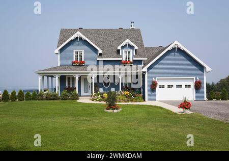 Blaue Holzdiele mit weißen Zierleisten zweistöckiges Haus mit landschaftlich gestaltetem Vorhof und Schottereinfahrt im Sommer. Stockfoto