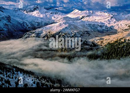 Der Morgennebel füllt das Tal zwischen den schneebedeckten, weißen Gipfeln der steifen und zerklüfteten San Juan Mountains. Silberne Schäfte, kein Sonnenlicht, gelockte Bergleute in... Stockfoto