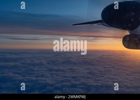 Atemberaubender Blick aus der Luft aus einem Flugzeug, zeigt einen Teil des Flügels und des Turbinenmotors, über den geschwollenen Wolken mit einem pastellfarbenen Himmel in der Dämmerung, Flug aus... Stockfoto