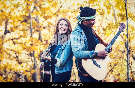 Gemischte Rasse verheiratete Paare, die sich zurücklehnen, Gitarren spielen während eines Familienausflugs in einem Stadtpark, während sie eine gute Zeit miteinander verbringen Stockfoto