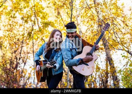 Gemischte Rasse verheiratetes Paar, das sich zurückhält, sich ansieht, lächelnd und Gitarren spielt, während eines Familienausflugs im Stadtpark, Spen... Stockfoto