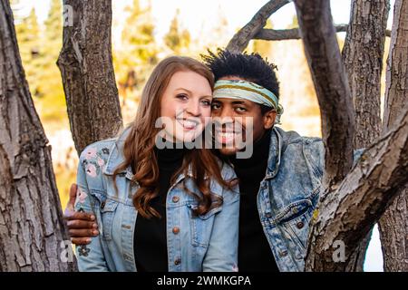 Nahaufnahme eines Paares gemischter Rassen, das die Kamera durch Äste umschließt und lächelt, während eines Herbstes zusammen verbringt... Stockfoto