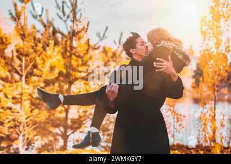 Ein Paar gemischter Rasse, Ehemann, der seine Frau in den Armen trägt und hält, während sie sich einen Kuss teilen und während einer Herbstfamilie Zeit verbringen... Stockfoto
