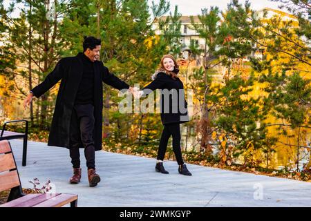 Ein gemischtes Paar von Rassen, das tanzt und Spaß hat, während es während eines Familienausflugs im Herbst in einem Stadtpark in Edmonton, Alberta, Kanada, gute Zeit miteinander verbringt Stockfoto