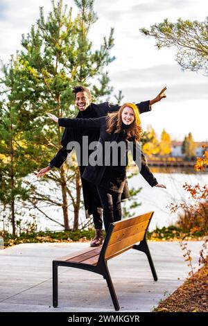 Porträt eines gemischten Rassenpaares, das auf einer Parkbank läuft, balanciert und lächelt in die Kamera, verbringt wertvolle Zeit zusammen während einer Herbstfamilie... Stockfoto