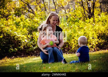 Mutter wirft einen Ball mit ihrer Tochter und ihrem kleinen Sohn, der an einem warmen Herbstnachmittag leidet, in einem Stadtpark; Leduc, Alberta, Kanada Stockfoto