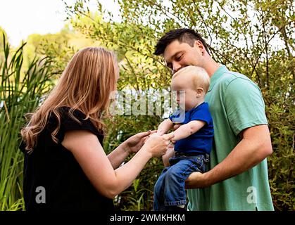 Mutter und Vater spielen mit ihrem kleinen Sohn, der an einem warmen Herbstnachmittag in einem Stadtpark leidet; Leduc, Alberta, Kanada Stockfoto