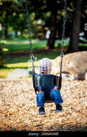 Junge mit Down-Syndrom, der an einem warmen Herbstnachmittag in einem Stadtpark schwingt; Leduc, Alberta, Kanada Stockfoto