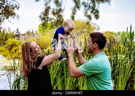 Mutter und Vater spielen mit ihrem kleinen Sohn, der an einem warmen Herbstnachmittag in einem Stadtpark leidet; Leduc, Alberta, Kanada Stockfoto