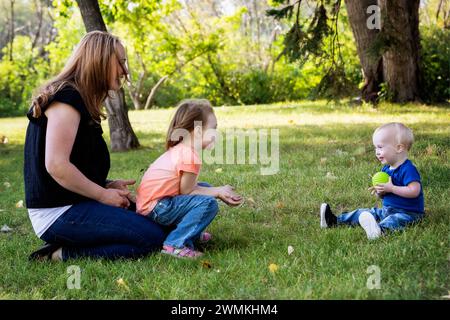 Mutter wirft einen Ball mit ihrer Tochter und ihrem kleinen Sohn, der an einem warmen Herbstnachmittag leidet, in einem Stadtpark; Leduc, Alberta, Kanada Stockfoto