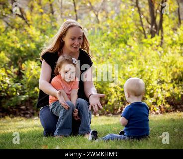 Mutter wirft einen Ball mit ihrem kleinen Sohn, der an dem Down-Syndrom leidet, und ihrer Vorschulertochter, während eines warmen Herbstnachmittags in einem Stadtpark Stockfoto