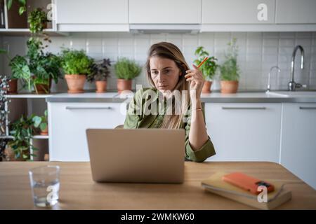 Beschäftigte, nachdenkliche Frau, die in der Küche sitzt, freiberuflich arbeitet, aufmerksam liest, denkt Stockfoto