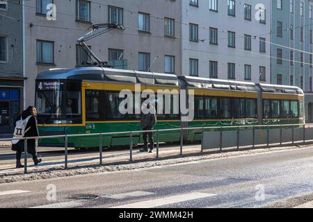 Mann raucht an der Straßenbahnhaltestelle Kansaneläkelaitos mit Straßenbahnlinie 4 im Hintergrund im Stadtteil Taka-Töölö in Helsinki, Finnland Stockfoto