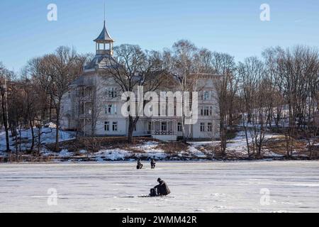 Eisfischer Eisfischer in der gefrorenen Töölönlahti Bay mit einer der Linnunlaulu Villen im Hintergrund in Helsinki, Finnland Stockfoto