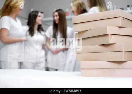 Ein Stapel brauner Catering-Boxen auf einem weißen Tisch in einem hellen Büro, mit medizinischem Fachpersonal im Hintergrund, was auf ein bevorstehendes Büro-fe hindeutet Stockfoto