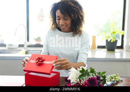 Birassische Frau öffnet eine Geschenkbox zu Hause während eines Online-Datums-Videoanrufs Stockfoto
