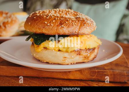 Eine Nahaufnahme eines Bagel Burgers mit Rührei, Spinat, Käse und Avocado auf einem Teller Stockfoto