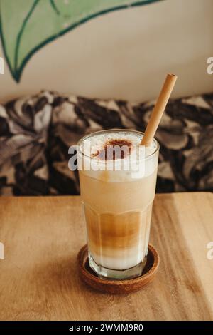 Nahaufnahme eines Cappuccinos in einem Glasbecher mit Bambusstroh auf einem Holztisch Stockfoto