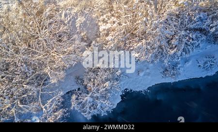 Ein schneebedeckter Wald entlang eines Flusses in einer Winterlandschaft Stockfoto