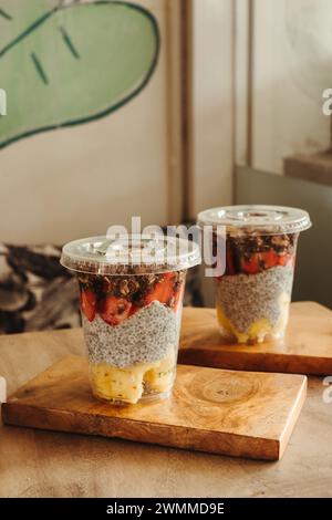 Zwei Puddings mit Obst, Müsli in einmachgläsern auf einem hölzernen Schneidebrett und ein grüner Smoothie in einer Tasse Stockfoto