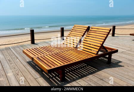 Zwei hölzerne Liegestühle auf einer Terrasse mit Blick auf das Meer Stockfoto