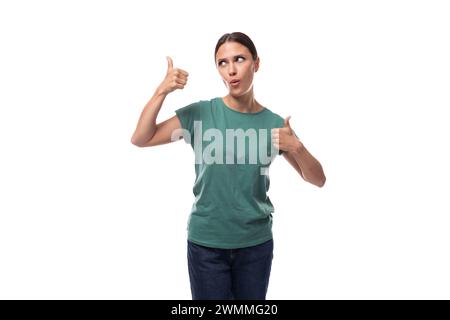 30 Jahre alte schlanke europäische Brünette mit einem Pferdeschwanz in einem grünen T-Shirt zeigt sich wie mit ihren Händen Stockfoto