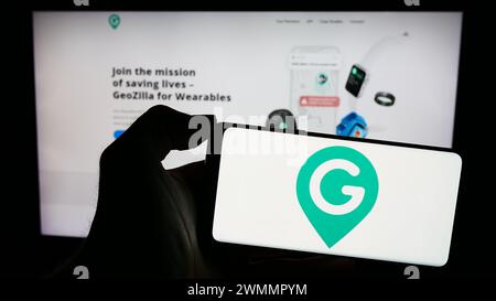 Person, die ein Mobiltelefon mit dem Logo des amerikanischen GPS-Ortungsunternehmens GeoZilla Inc. Vor der Webseite hält. Schwerpunkt auf dem Display des Telefons. Stockfoto