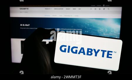 Person, die ein Mobiltelefon mit dem Logo des taiwanesischen Computerhardware-Unternehmens Gigabyte Technology vor der Webseite hält. Schwerpunkt auf dem Display des Telefons. Stockfoto