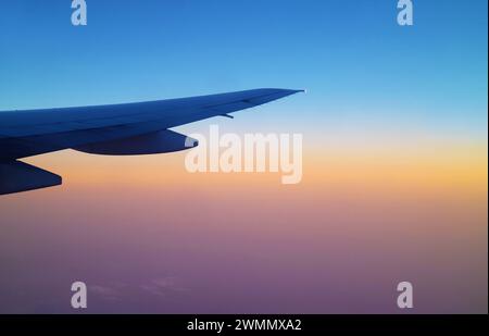 Atemberaubender Sonnenaufgangshimmel mit Flugzeugflügel aus dem Flugzeugfenster während des Fluges Stockfoto