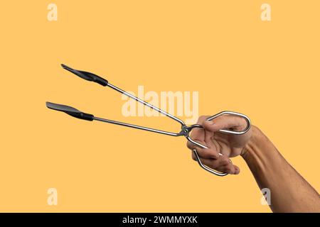 Männliche Hand, die Küchenzange isoliert auf gelbem Hintergrund hält Stockfoto
