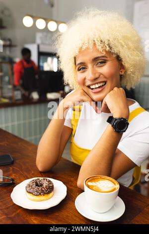 Eine junge Frau, die eine Rasse hat, genießt einen Kaffee und Donut in einem Café Stockfoto