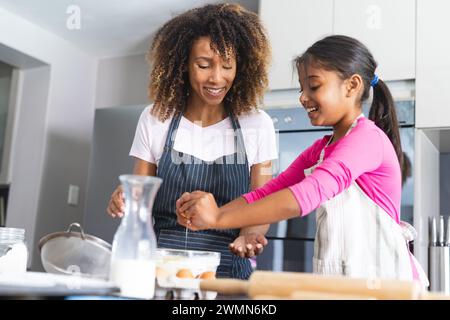 Birassische Mutter und Tochter genießen es, gemeinsam zu Hause für ihre Tochter zu backen. Sie teilen einen freudigen Moment, während sie ein hausgemachtes Rezept zubereiten. Stockfoto