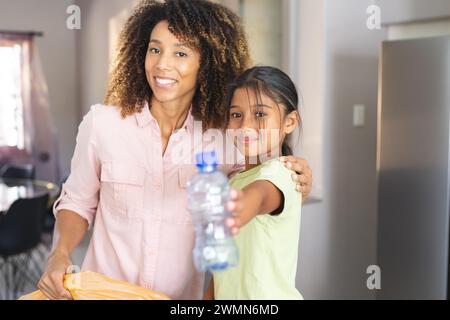 Birassische Mutter lächelt zu Hause in einer Küche und zeigt eine Plastikflasche. Sie teilen einen Moment der Bindung und fördern gleichzeitig gesunde Hydration. Stockfoto