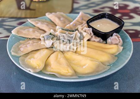 Gekochte Teigtaschen mit verschiedenen Füllungen auf einem Teller mit Sauerrahmsauce auf dem Tisch in einem Restaurant Stockfoto