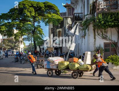 Zwei Träger bewegen einen beladenen Trolley mit Säcken vom Fährterminal in Stone Town, Sansibar, Tansania Stockfoto