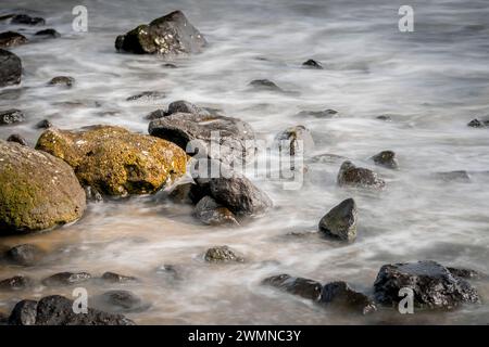 Malerischer Blick auf raue Felsformationen im schaumigen Meerwasser mit moosigen runden Felsbrocken in der Nähe der Küste Stockfoto
