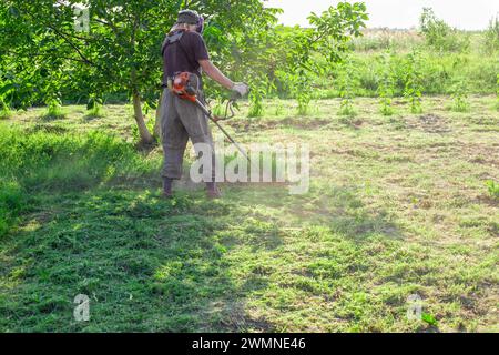 Mähen des Grases, Pflege des Gartens. Ein Mann mäht Gras mit einem Benzinmäher im Garten an einem Sommertag. Stockfoto