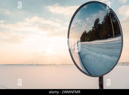 Konvexer Spiegel, der die Winterstraße reflektiert. Schneebedeckte Landschaft im Hintergrund Stockfoto