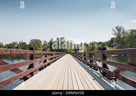 Schwindender perspektivischer Blick auf die Holzbrücke über einen See. Symmetrischer Blick auf die Steg-Brücke in der Landschaft an einem sonnigen Tag. Stockfoto