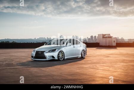 Lexus IST EINE Limousine, die auf der obersten Etage des Parkhauses geparkt wird. Goldenes Sonnenuntergangslicht. Skyline der Stadt im Hintergrund Stockfoto