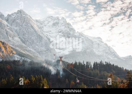 Kleine rote Seilbahn auf der Bergbahn, die Passagiere auf die Zugspitze hinaufbringt. Rauch im Bergwald in der Nähe der Seilbahn. Stockfoto