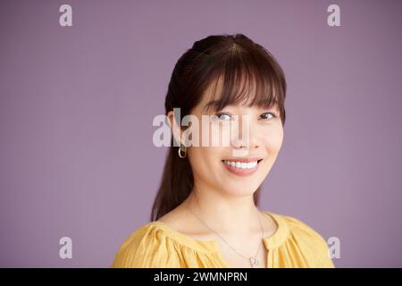 Porträt einer fröhlich lächelnden vietnamesischen Frau, die an einer Fliederwand steht Stockfoto