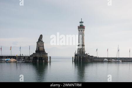 Leuchtturm und Löwenstatue am Eingang zum halb leeren Hafen an einem bewölkten Morgen. Das andere Ufer des Sees ist von Nebel bedeckt. Stockfoto