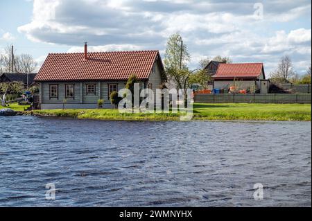 Alte Holzhäuser am Ufer des Flusses im Dorf an einem bewölkten Frühlingstag. Stockfoto