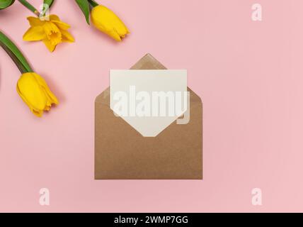 Draufsicht der gelben Tulpen und Narzissen auf rosa Hintergrund. Kraftumschlag, weiße Karte. Farbenfrohe Komposition im Frühling, flacher Lay, Kopierraum. Stockfoto