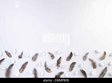 Blick von oben auf braune Federn, weiße ostereier auf weißem Hintergrund. Kreative osterkomposition, Frühling, Kopierraum, flache Lay. Stockfoto