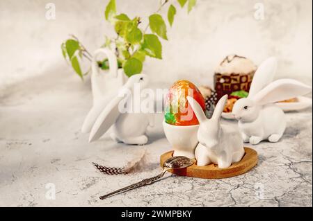 Frühlingsstillleben mit einem bemalten Ei, Osterhasen, Schokoladen-Cupcake und Eiern mit zartem Farbmuster auf dem Tisch. Osterdekor im Haus Stockfoto
