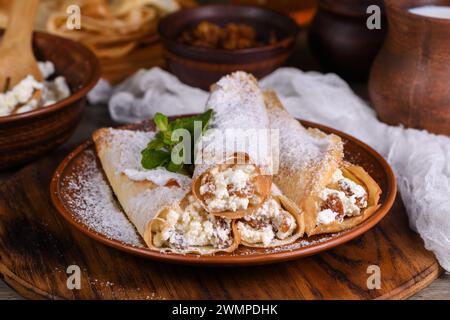 Dünne Pfannkuchen gefüllt mit Hüttenkäse, Honig und Rosinen, in Form eines Röhrchens gerollt, mit Puderzucker bestreut, mit Minze garniert. Festlich Stockfoto